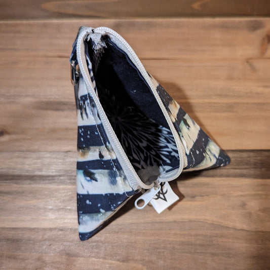 A D4 shaped bag with snowy birch print fabric outside has a white zipper up the middle open to show a white snowflake pattern on a navy liner.