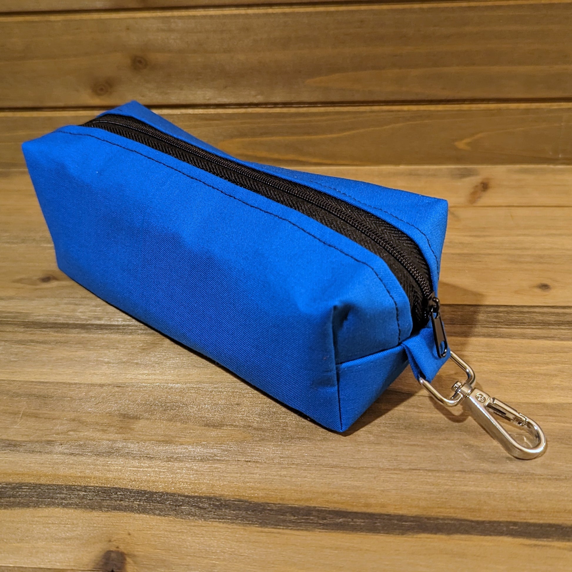 A view of the blue Bag of Devouring with a black zipper down the middle and a keychain clip at the top.