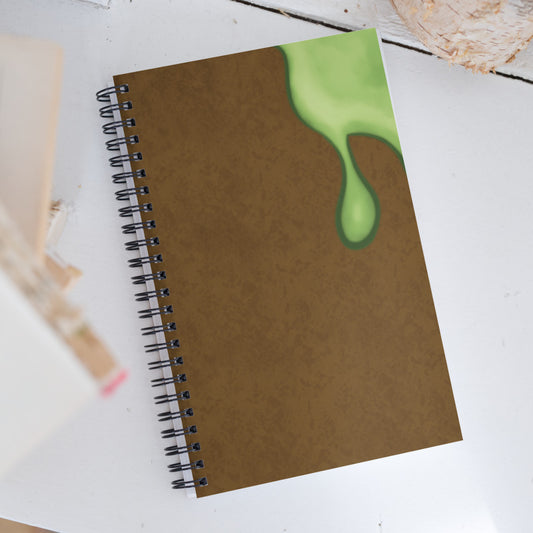 A spiral notebook with a brown tonal texture and a green slime blob illustration on one side with 3 dimensional shading.