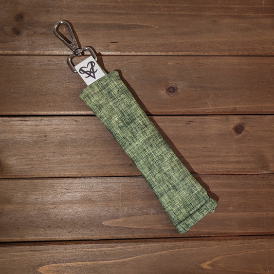 A pen length bag with a keychain clip at the top and a squeeze open on the other side is made with sage green linen print fabric.