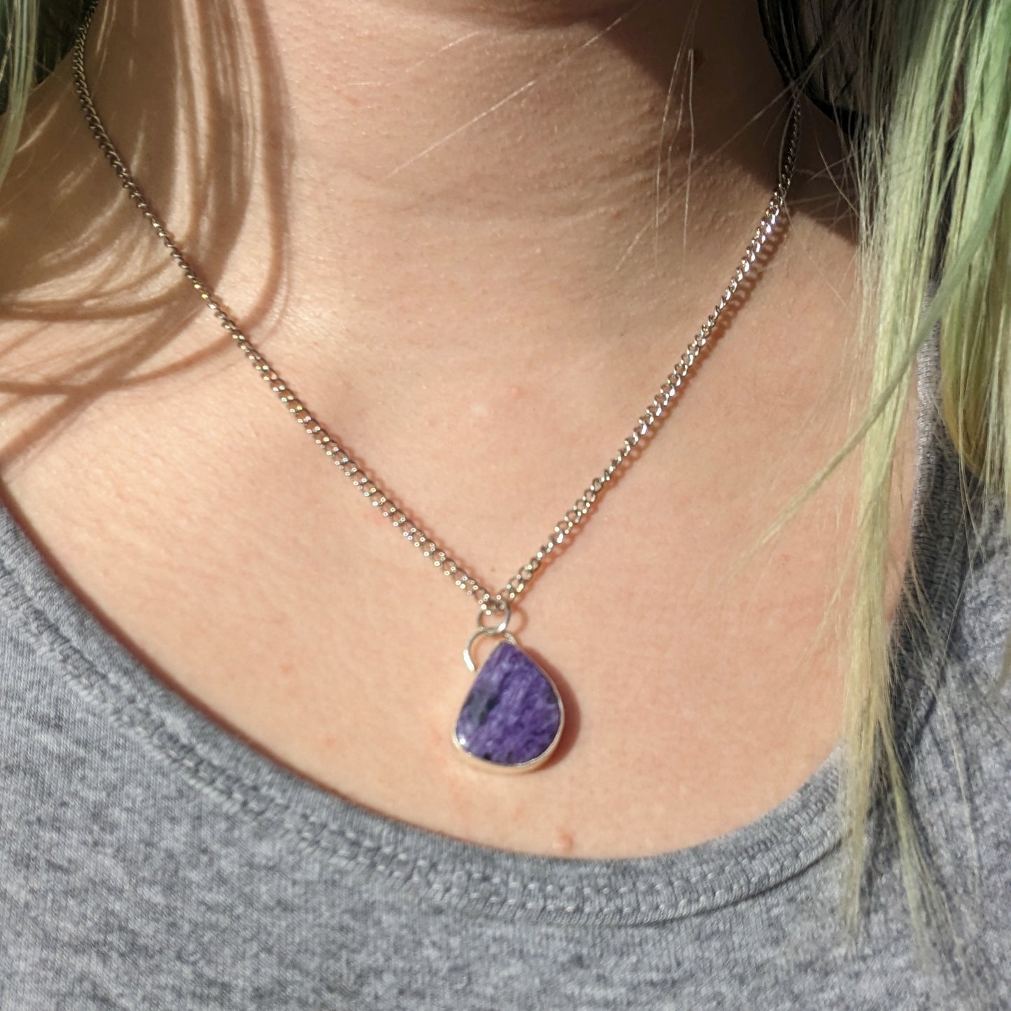 Aras models the purple charoite necklace to show how it hangs similarly to a teardrop pendant but off center due to the asymmetrical nature of the stone.