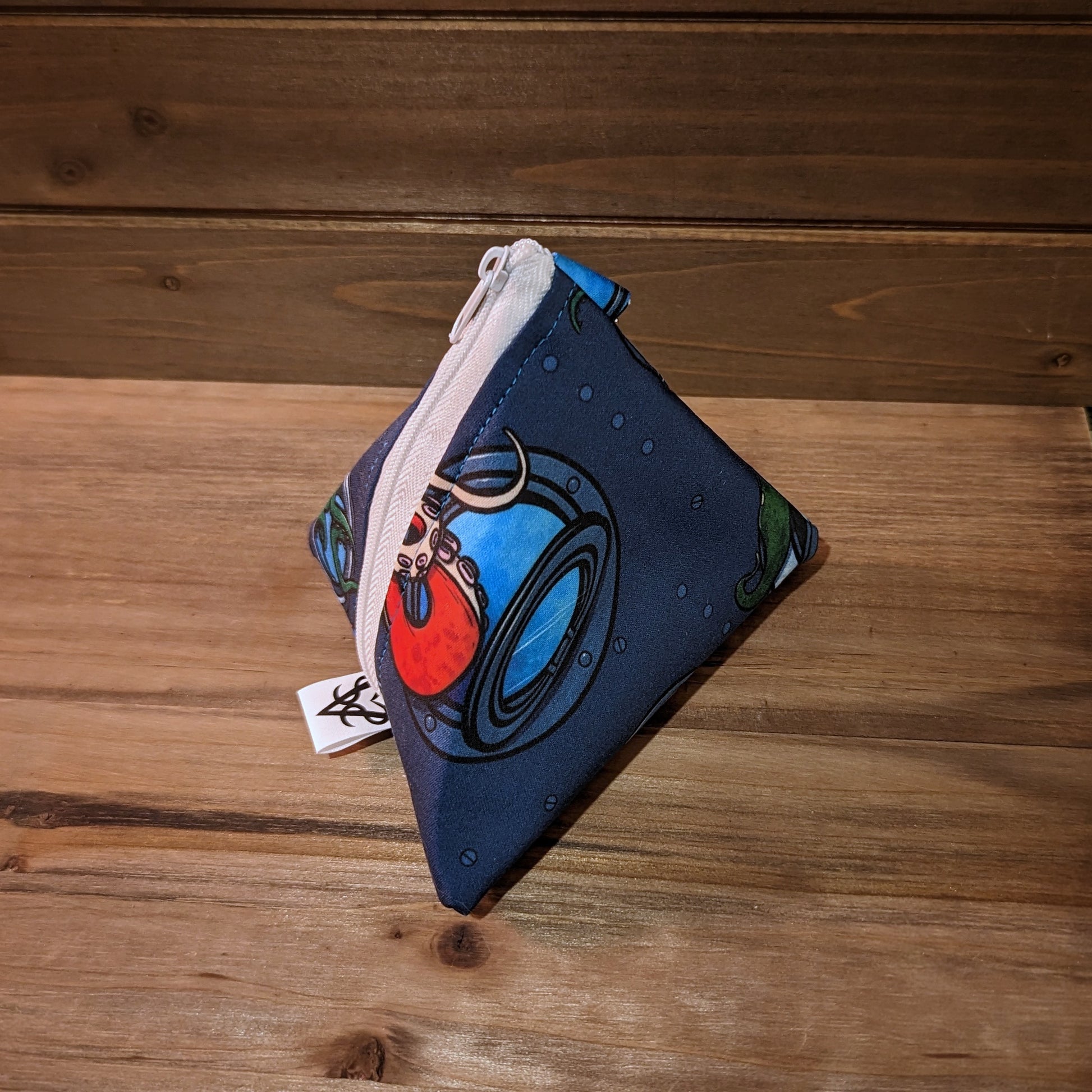 A 5 inch D4 bag has an print that looks like the inside of a submarine with tentacles breaching portholes near a nervous looking fish, a white zipper, and a keychain clip.