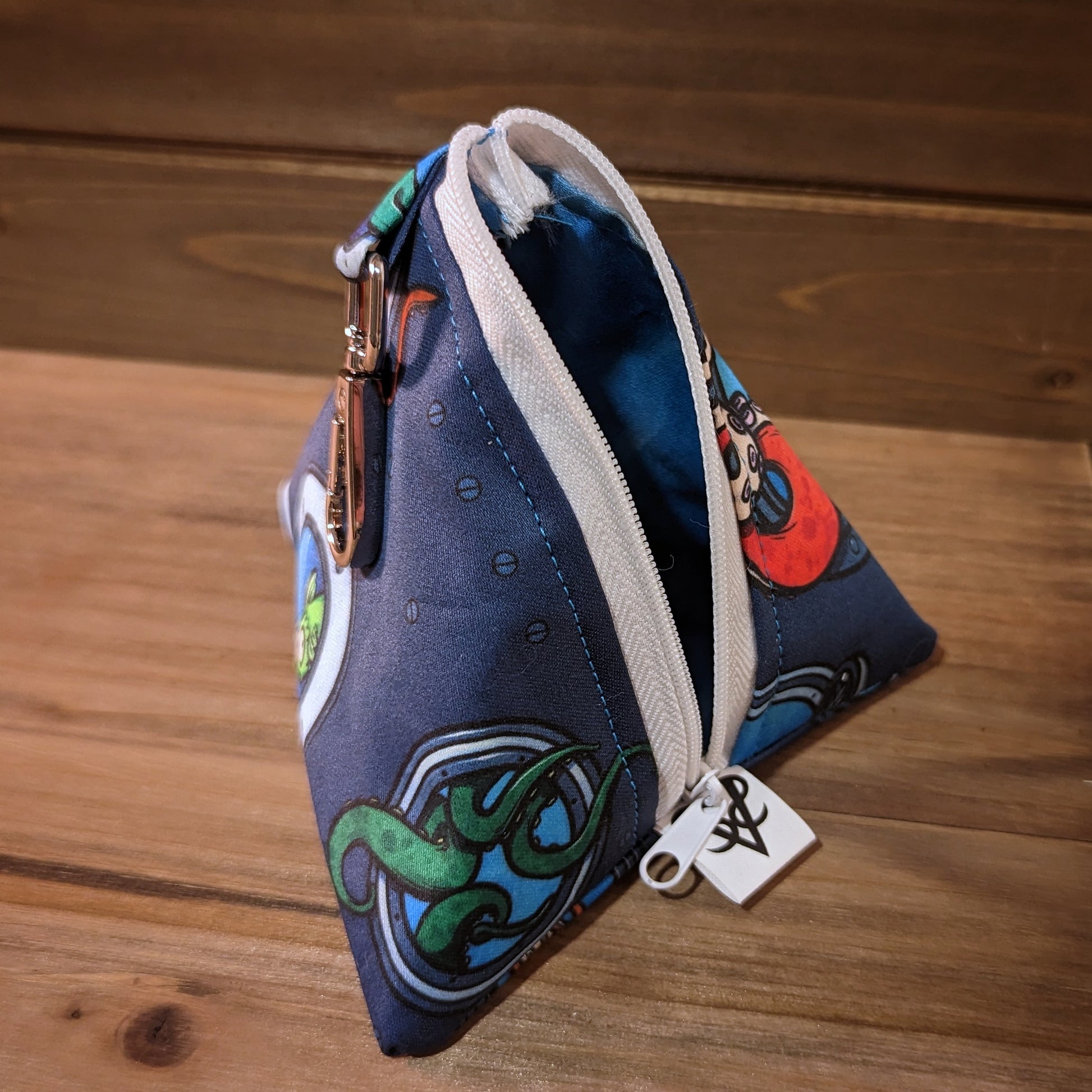 A 5 inch D4 bag has an print that looks like the inside of a submarine with tentacles breaching portholes near a nervous looking fish, a white zipper open to show a water print interior, and a keychain clip.