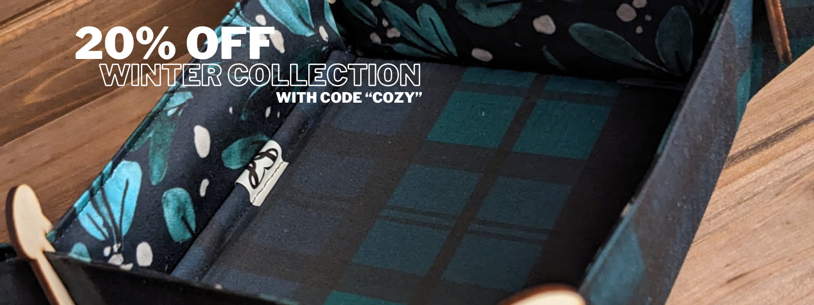 A dice tray with green and blue plaid and white mistletoe print fabric with writing saying 20% off Winter Collection with code "cozy".