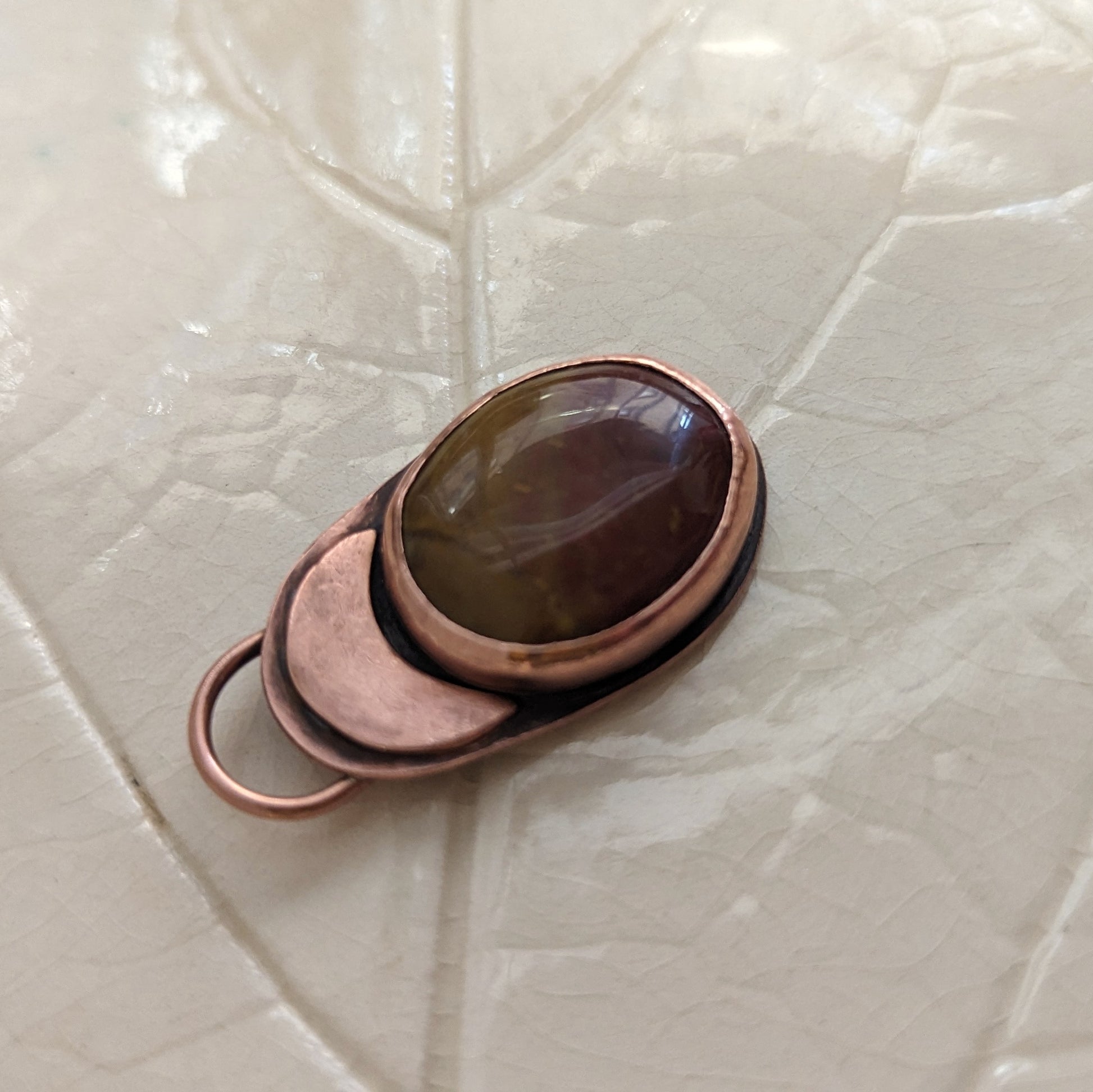 A deep red and ochre agate stone is set in copper under a copper moon.