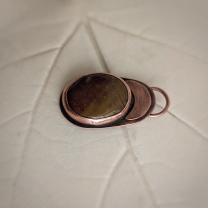 A deep red and ochre agate stone is set in copper under a copper moon.