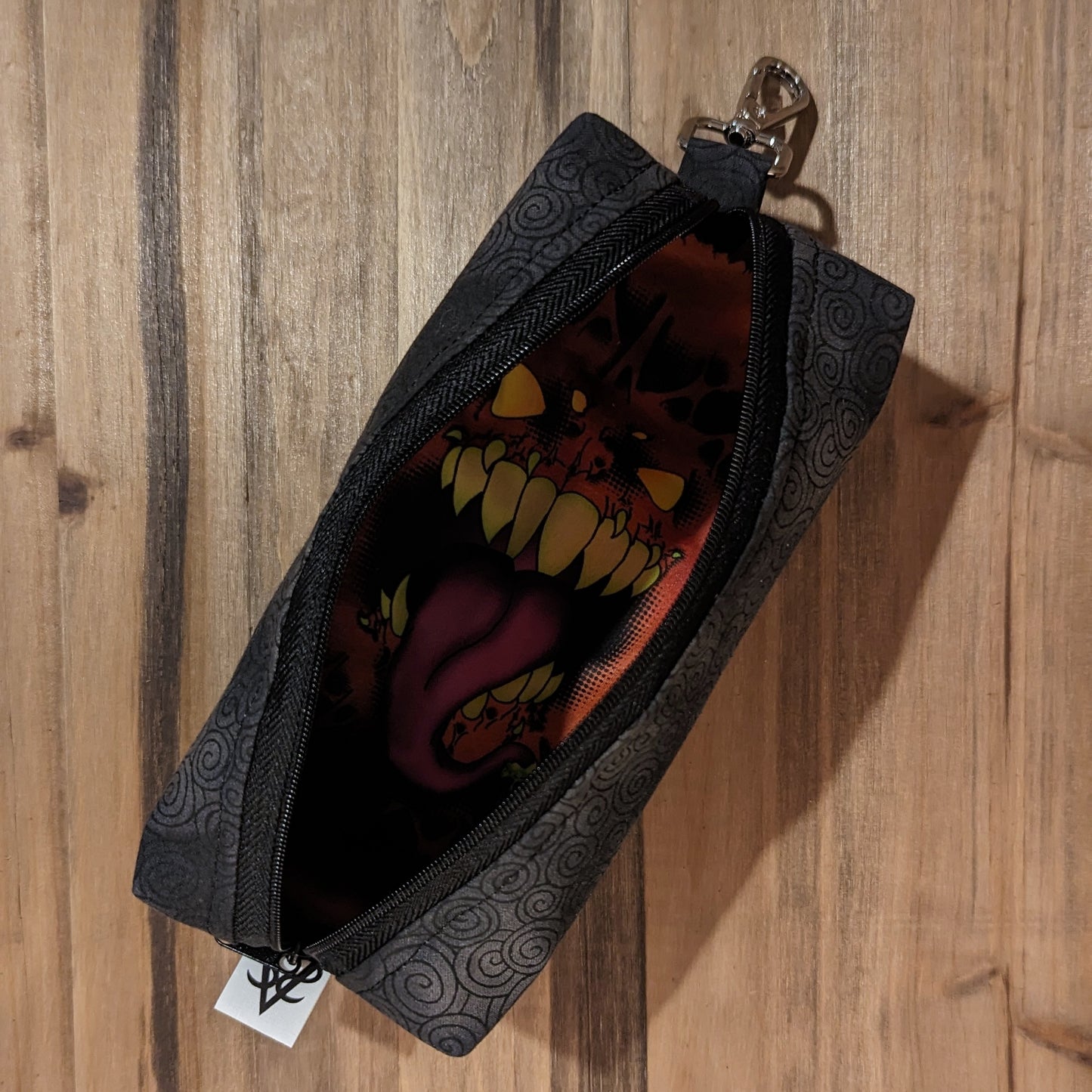 The Bag of Devouring in the spiraling black open to show the mimic face inside, the keychain clip at the top, and the Aras Sivad Studio tag at the bottom.