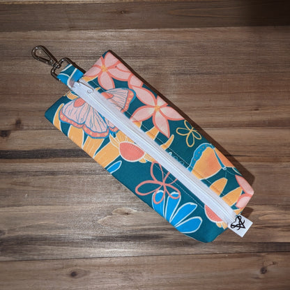 A long skinny fabric bag with bright flowers and butterflies has a keychain clip at the top, white zipper in the middle, and a box bottom.