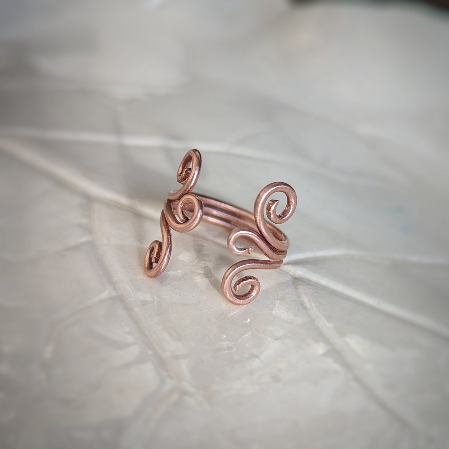 An adjustable copper ring consisting of three wires soldered together, each side ending in graceful swirls shines bright in the daylight.