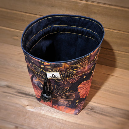 A drawstring bag has gold and pink gingko leaves, golden stitching, and a blue tonal liner.