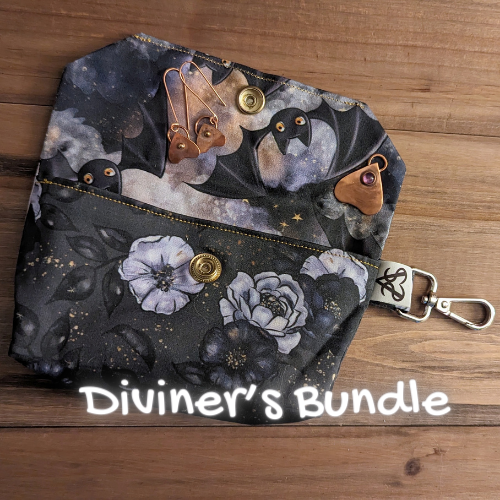 A tarot case with a rose print outside and a cute pat print inside has a pair of copper planchette earrings and an amethyst set planchette pendant on it and Diviner's Bundle written in glowing handwriting.