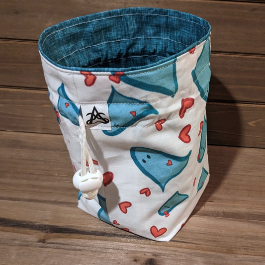 A drawstring bag has white fabric outside printed with teal ghosts and red hearts and a coordinating hatch mark liner.