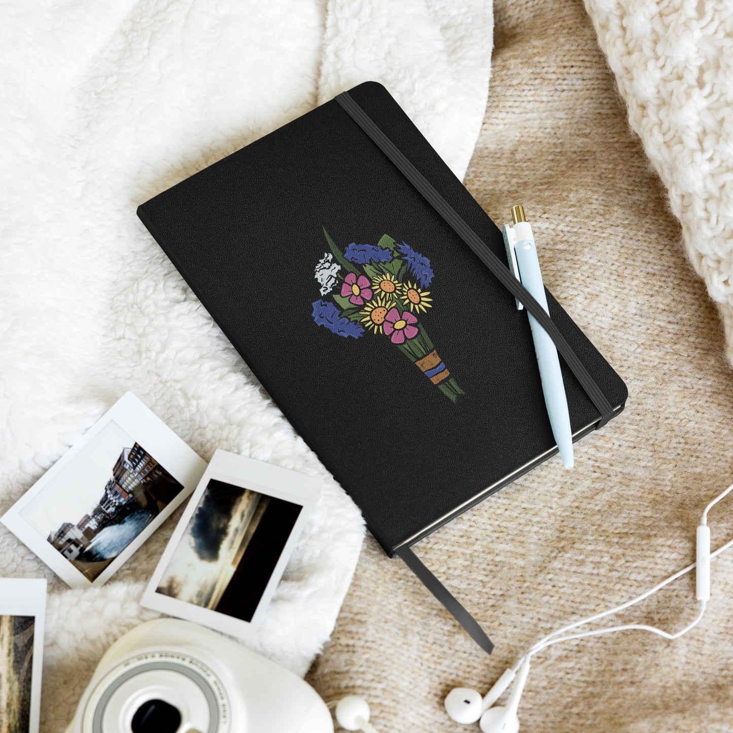 A black hardcover notebook has a flat colored bouquet of flowers by Aras Sivad on the cover, a ribbon hanging out the bottom, and a pen stuck in its elastic closure.