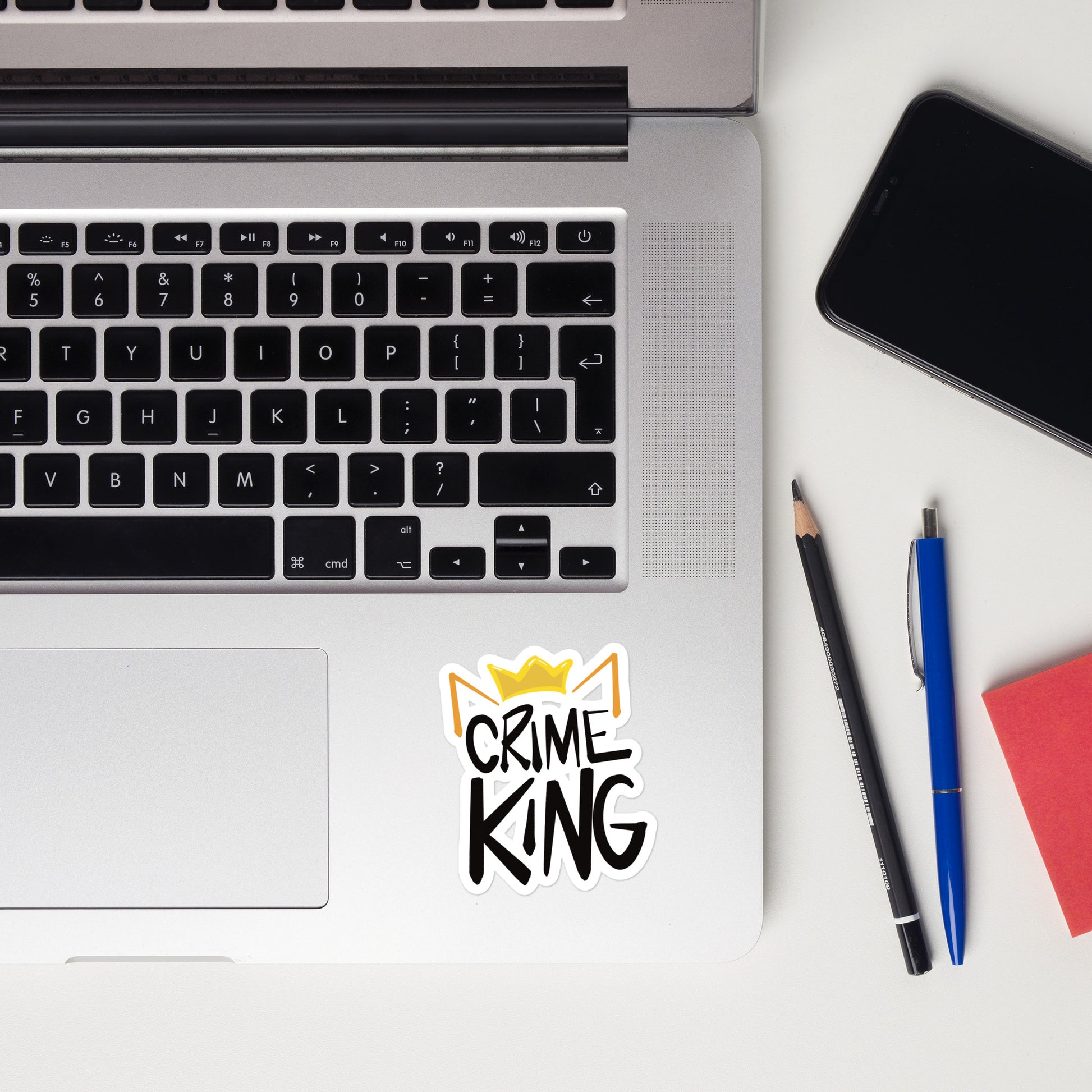 A sticker on a laptop has orange cat ears and a yellow crown over the words "Crime King" in bold writing.