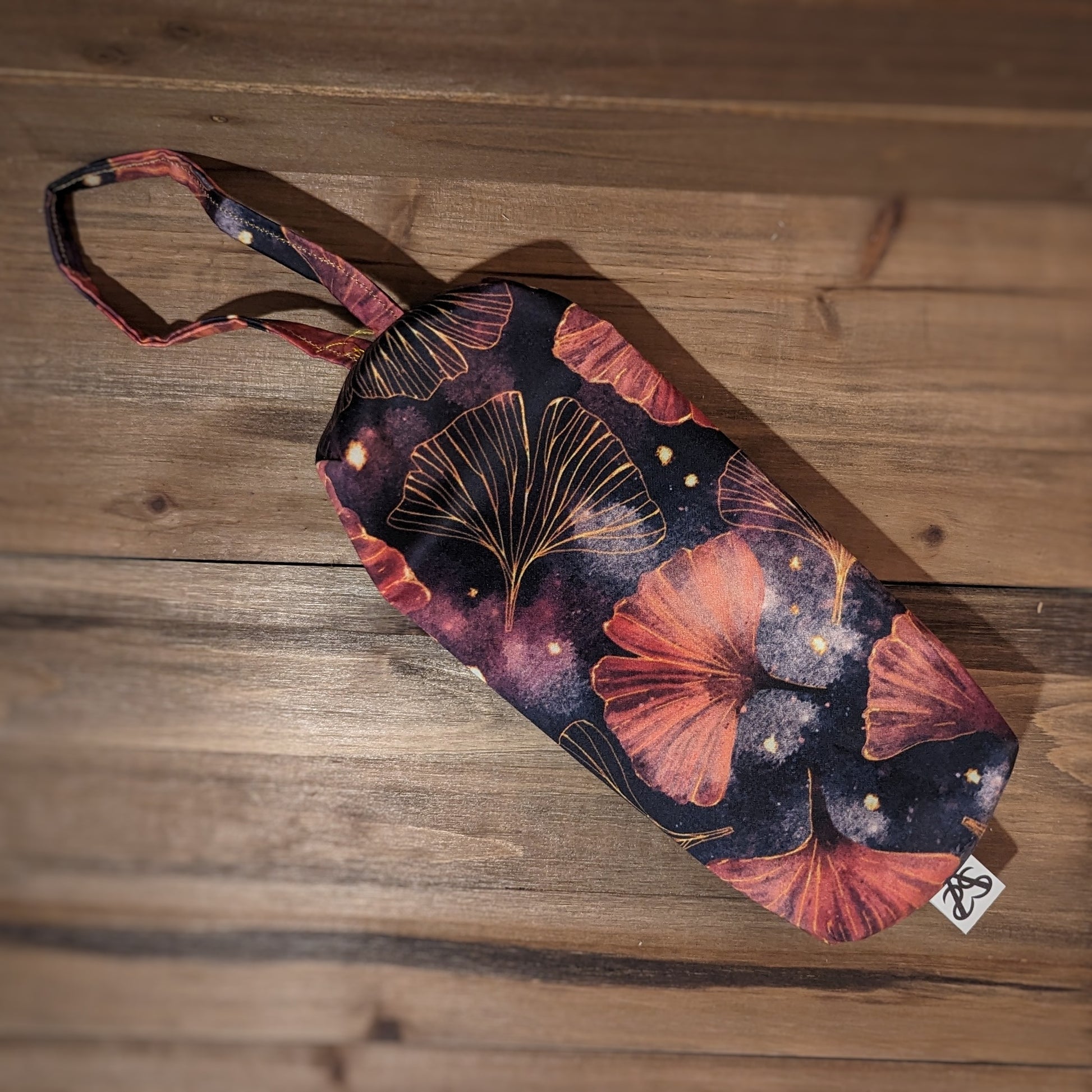 A long skinny pencil case is turned over to show the gold and pink gingko print back with matching wrist strap.