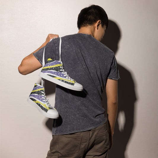 A model holds a pair of high-top shoes with ribbons of the yellow, purple, and black of the non-binary pride flag coming from the heel and expanding towards the laces with an explosion of stars over it by the white strings