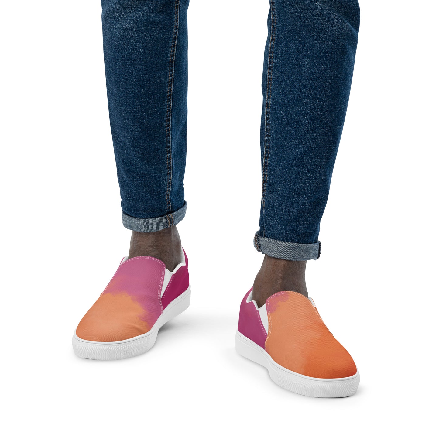 Front view: A model wears a pair of slip on canvas shoes with the colors of the lesbian pride flag in a cloudy texture, a white heart on the side, and the Aras Sivad logo on the back.