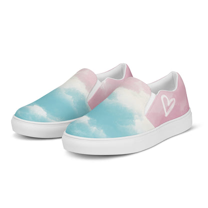 Left front view: A pair of slip on shoes has a cloud pattern with color blocked areas of blue, white, and pink, a white doodled heart on the outside, and the Aras Sivad Studio logo on the heel.