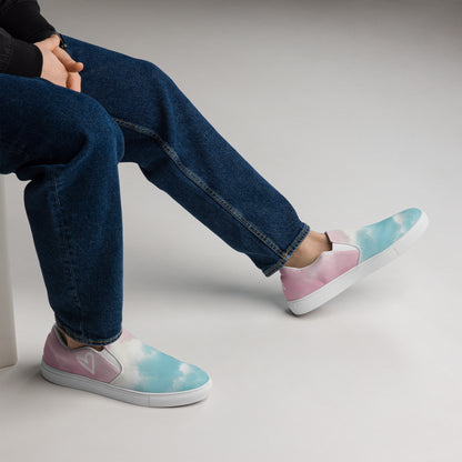 A model wears the Cloudy Transgender Pride flag slip on shoes with pink, white, and blue color block clouds, white heart, and white details.