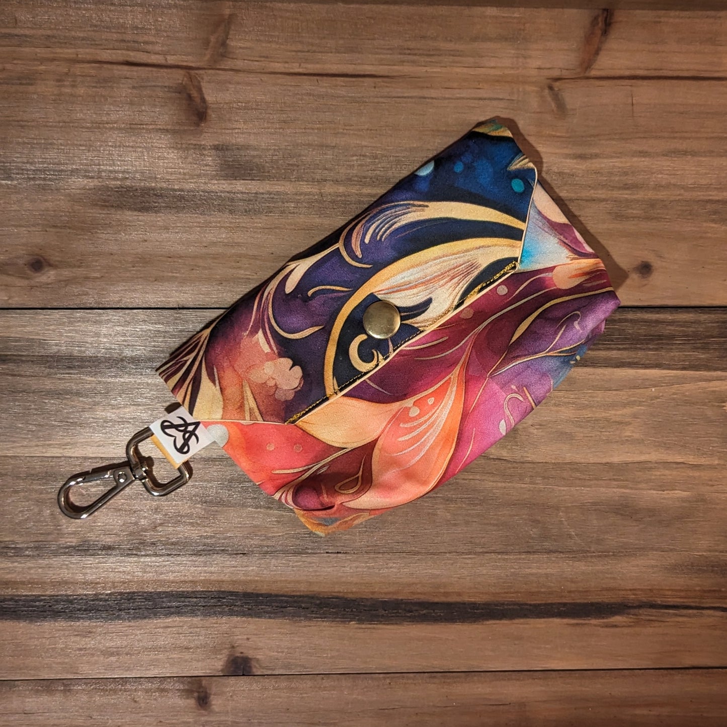 A bright tarot card case with swirling pinks, oranges, blues, purple, and gold outside, a keychain clip, and a gold snap close.