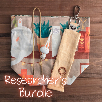 The Familiar Bookshelf drawstring bag has a gold brass hammered book fork, a yellow keychain bag, and a copper triple ring on it, Researcher's Bundle written in glowing hand over the photo.
