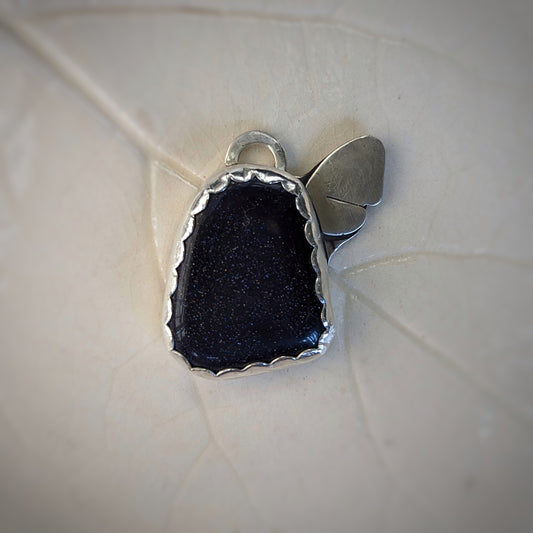 A silver pendant has a blue sandstone set in a scalloped edge bezel with a dainty silver moth resting on one side of the irregularly shaped stone.