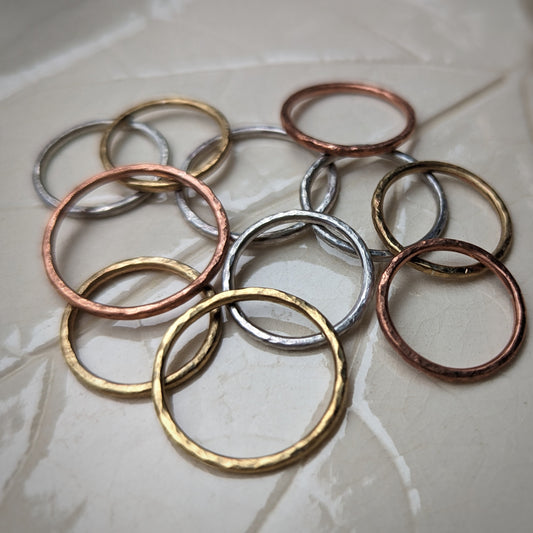 A collection of rings in gold brass, pink copper, and silver sit scattered on a leaf imprint tray.