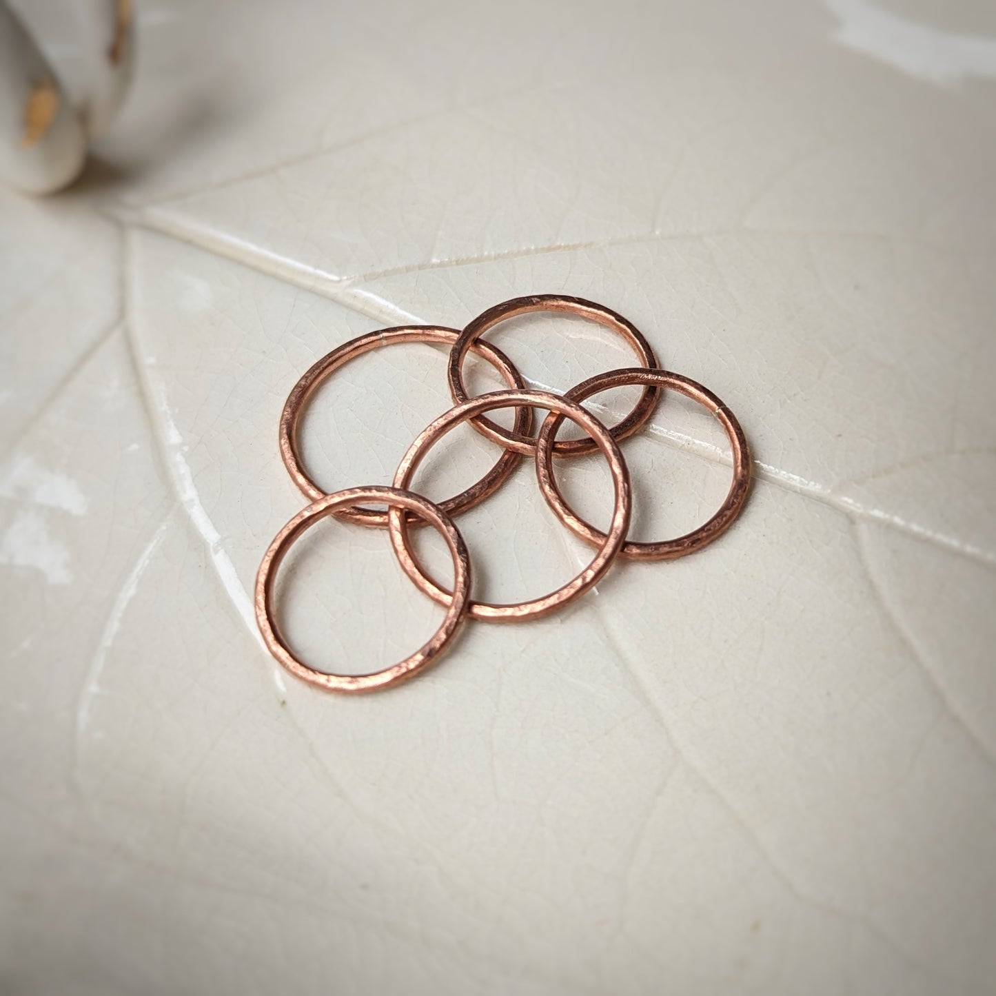 A collection of hammer texture pink copper rings sit scattered on a leaf imprint tray.