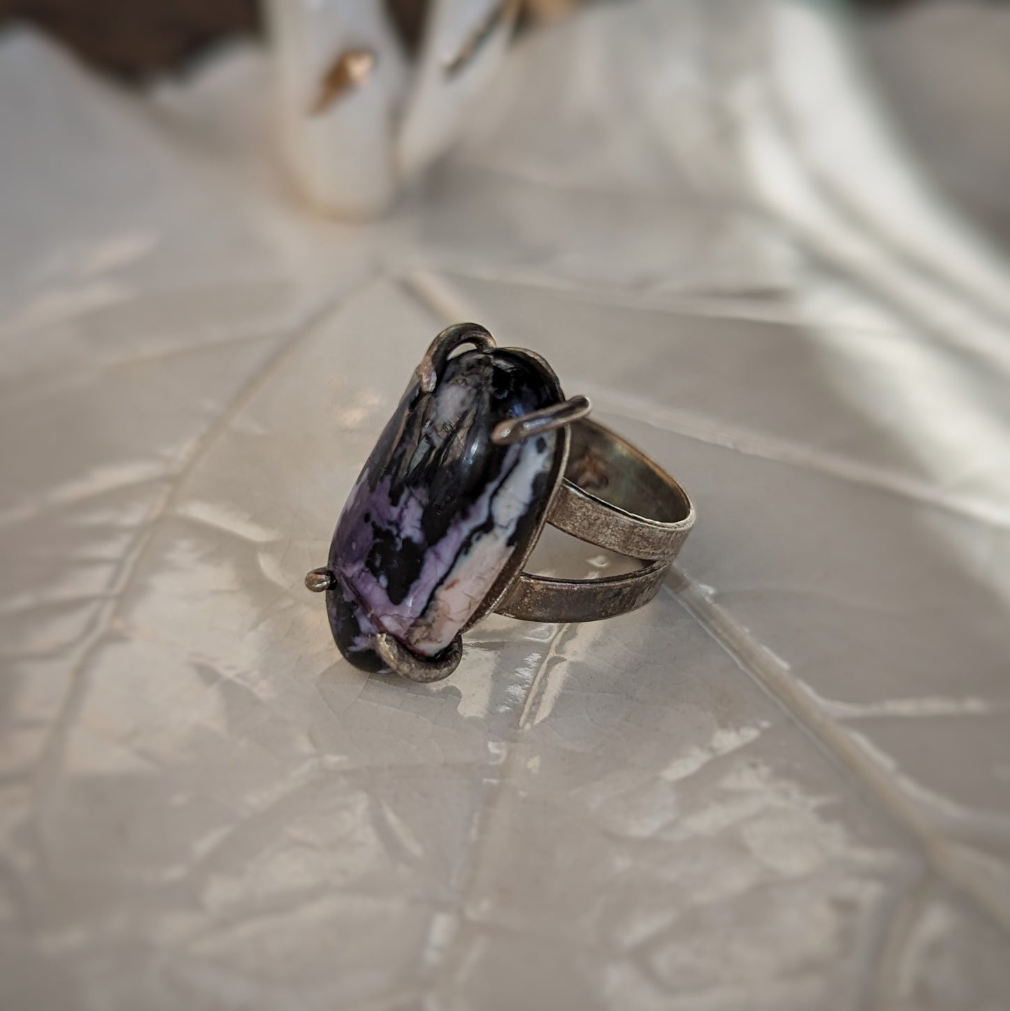 An oxidized silver ring has an oval purple jasper stone cabochon in a prong setting on a wide split shank band.