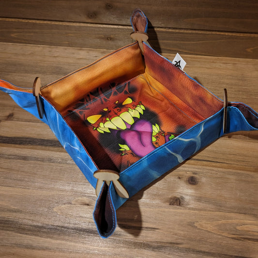 A dice tray has a mimic face print inside with glowing yellow eyes and a big purple tongue and a water print outside.