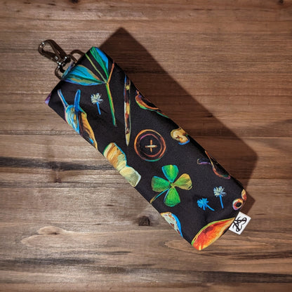 A long bag with box ends has a colorful forest pattern with pinecones, snails, frogs, acorns, florals, and keys, flipped over to show the back of the bag.