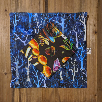 The witch's forest deluxe tray laid flat to show the two pieces flat. One side is a blue tonal tree design and the other side is a brightly colored item scatter including mushrooms, bees, snails, crystals, and acorns.