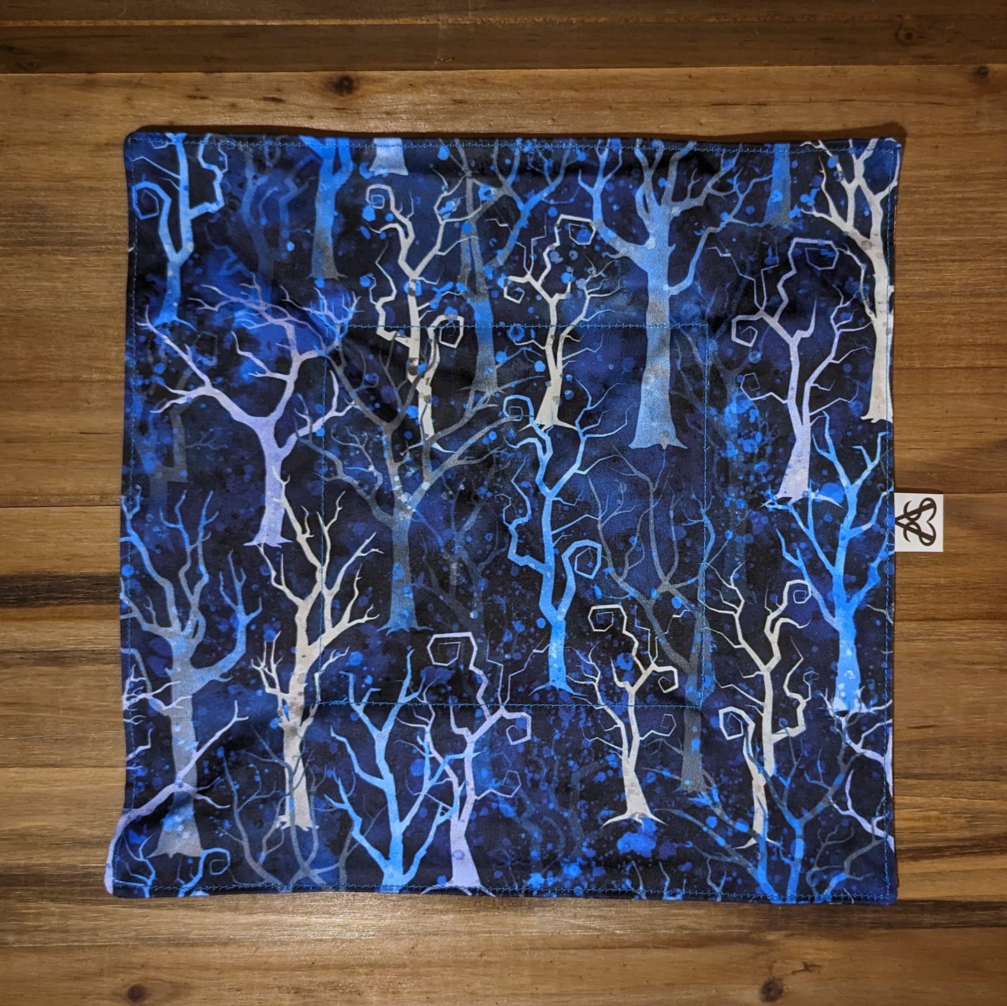 The witch's forest tray laid flat to show the spindly blue tone trees on the other side with the blue stitches that fade more into the blues of the pattern.