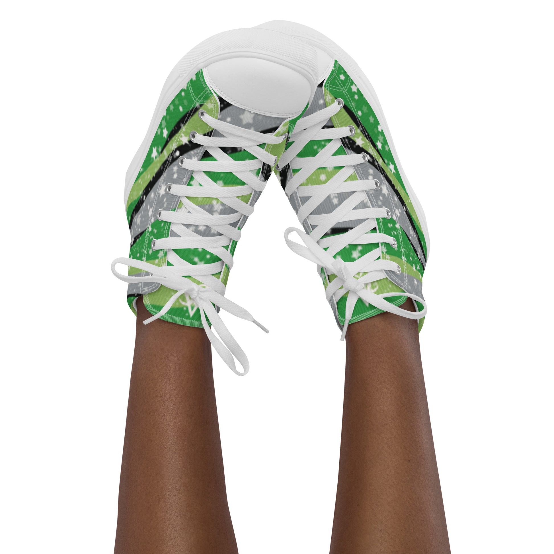A model wears a pair of high-top shoes with ribbons of the greens, grey, and black of the aromantic pride flag coming from the heel and expanding towards the laces with an explosion of stars over it, white accents, and the Aras Sivad Studio logo in white on the tongue.