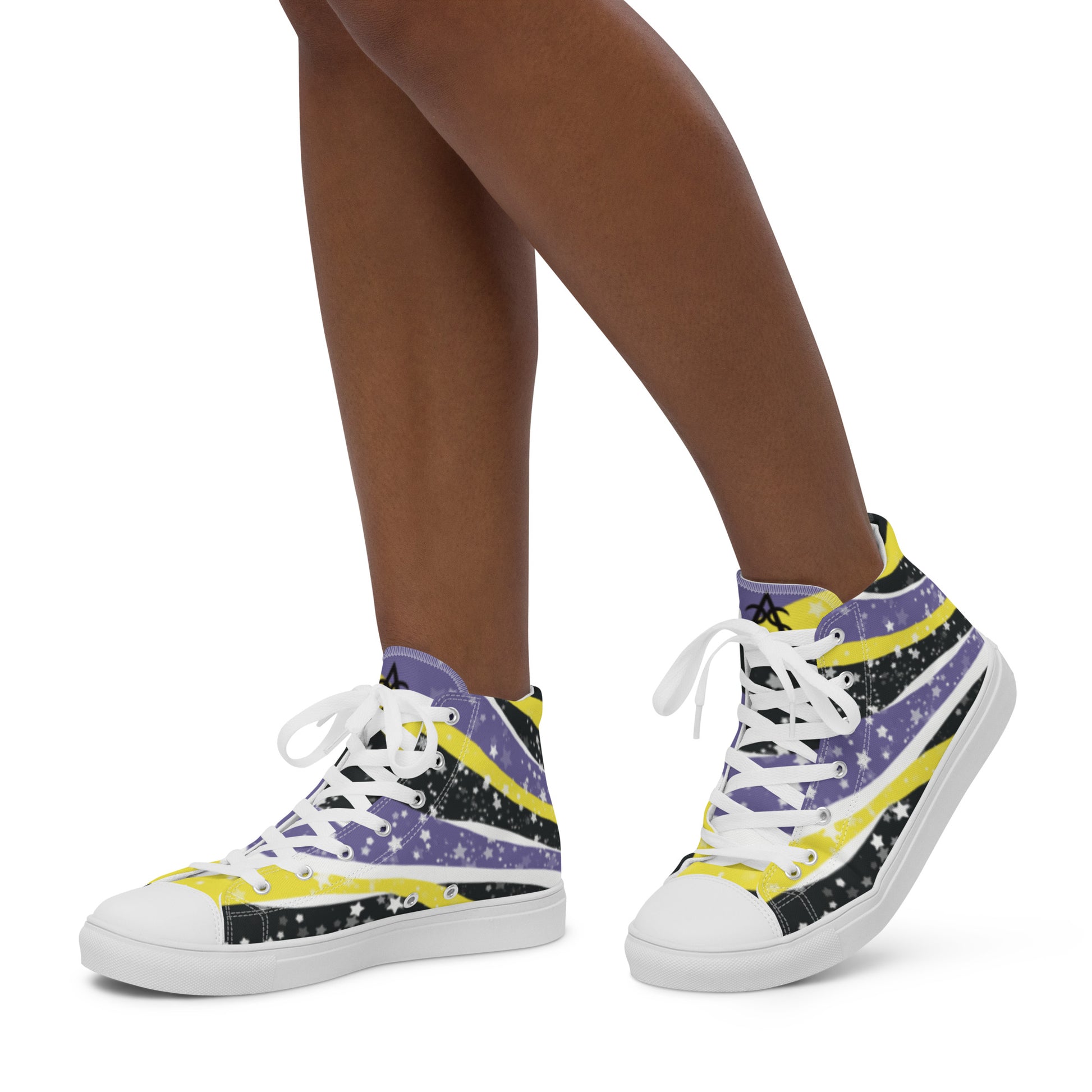A model wears a pair of high-top shoes with ribbons of the yellow, purple, and black of the non-binary pride flag coming from the heel and expanding towards the laces with an explosion of stars over it, white accents, and the Aras Sivad Studio logo in black on the tongue.
