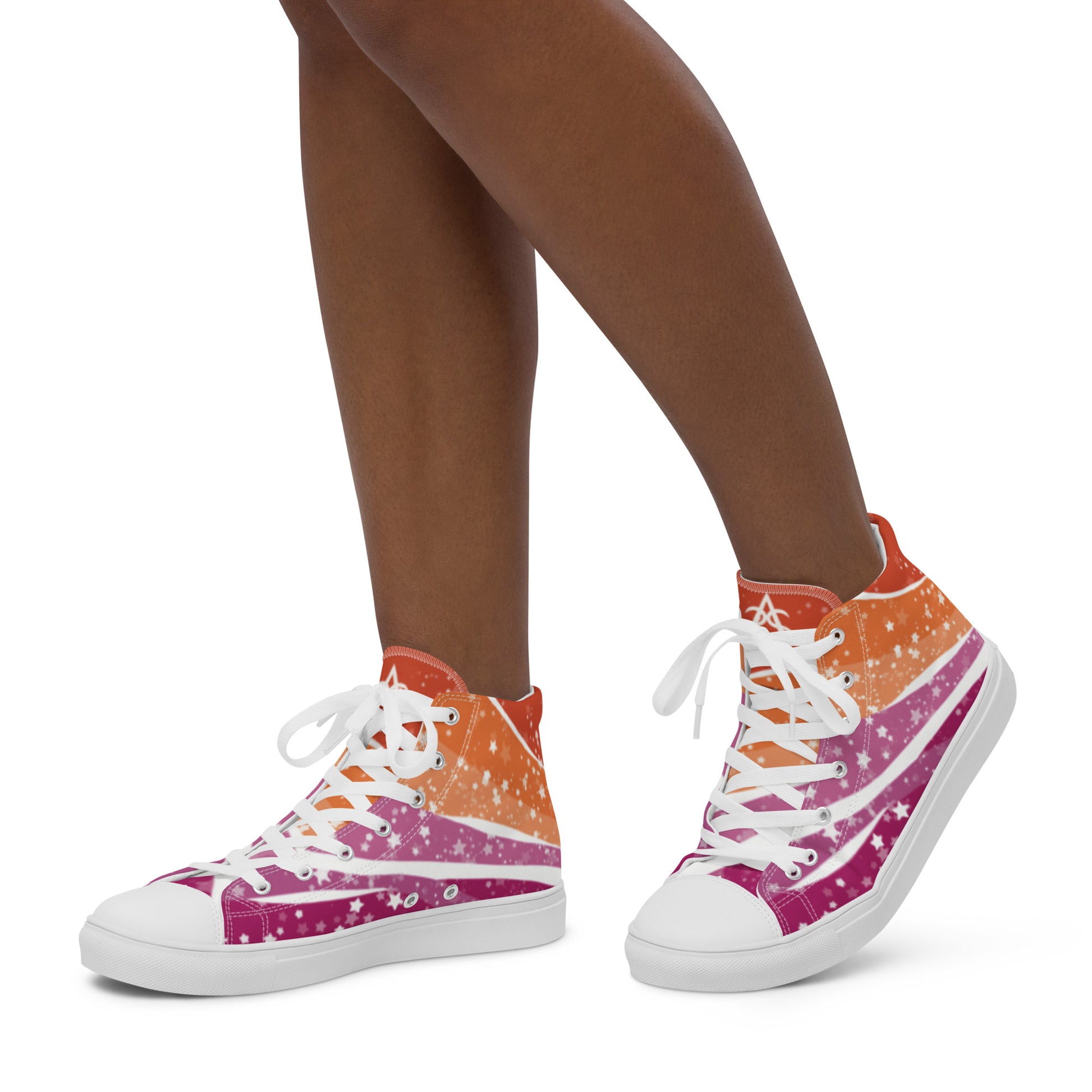 A model wears a pair of high top shoes with ribbons of lesbian flag colors and stars coming from the heel and getting larger across the shoe to the laces.