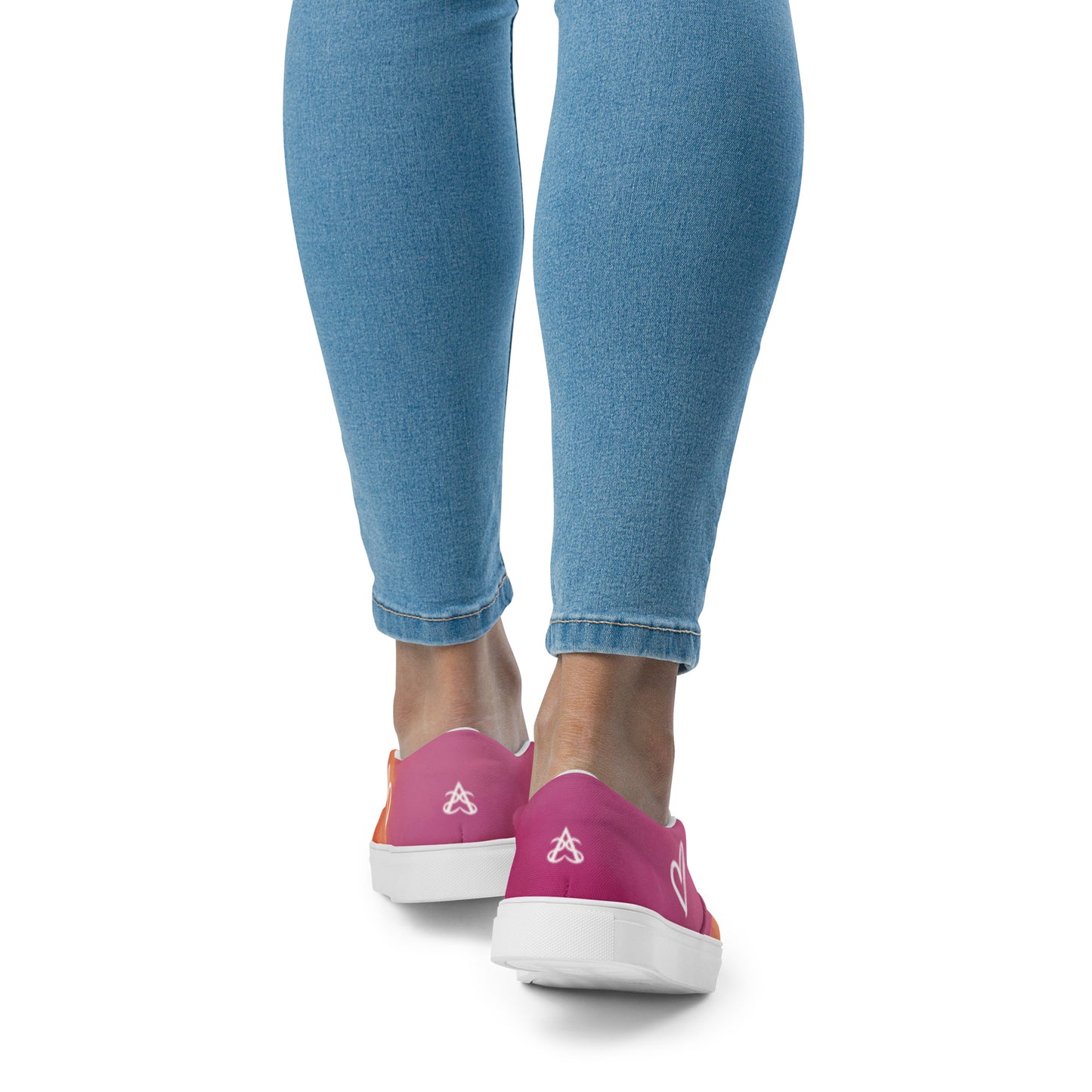 Back view: A model wears a pair of slip on canvas shoes with the colors of the lesbian pride flag in a cloudy texture, a white heart on the side, and the Aras Sivad logo on the back.