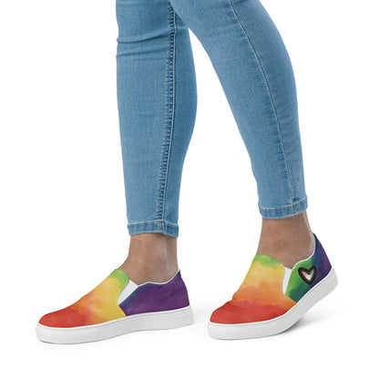 A model wears the Cloudy Rainbow Pride slip on shoes.
