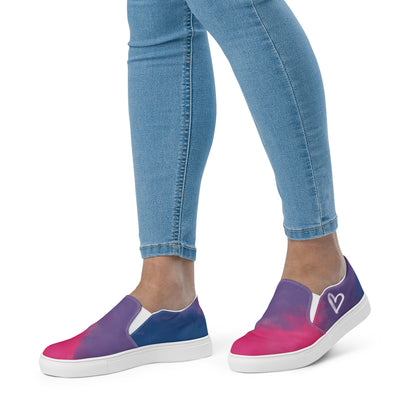 A model wears a pair of slip on shoes with color block pink, purple, and blue clouds, a white hand drawn heart, and the Aras Sivad logo on the back.
