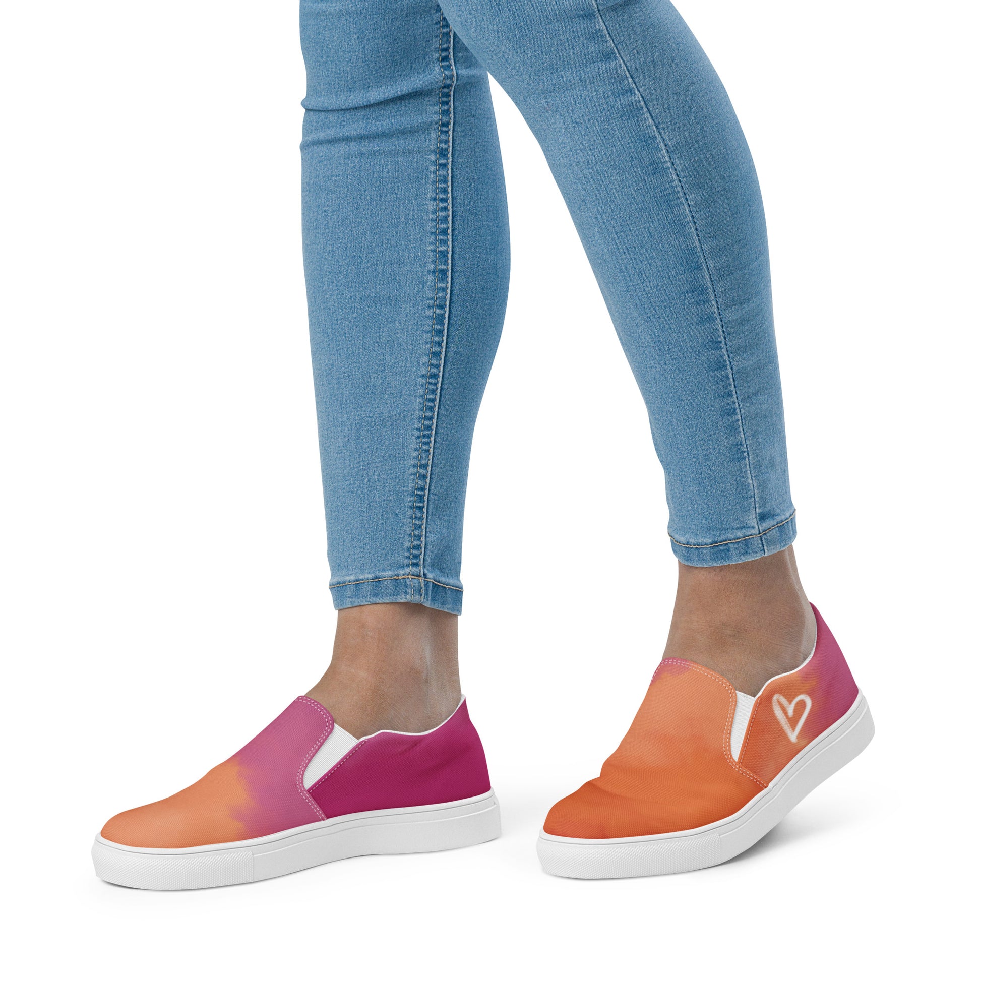 Left view: A model wears a pair of slip on canvas shoes with the colors of the lesbian pride flag in a cloudy texture, a white heart on the side, and the Aras Sivad logo on the back.