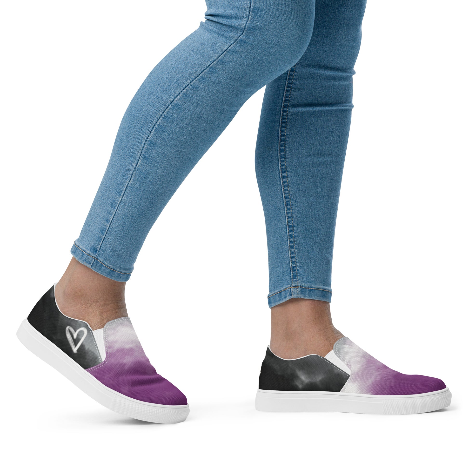 A model wears a pair of slip-on shoes with clouds in the asexual flag colors, a hand drawn white heart on the side, and the Aras Sivad Studio logo on the back.