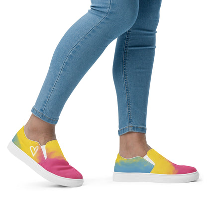 A model wears a pair of slip on shoes with color block pink, yellow, and blue clouds, a white hand drawn heart, and the Aras Sivad logo on the back.