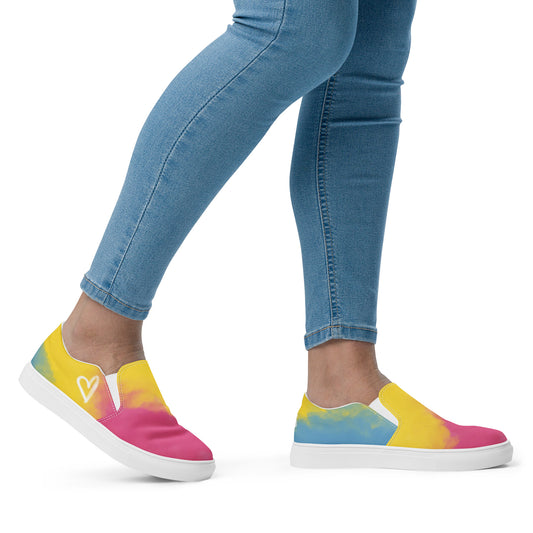 A model wears a pair of slip on shoes with color block pink, yellow, and blue clouds, a white hand drawn heart, and the Aras Sivad logo on the back.