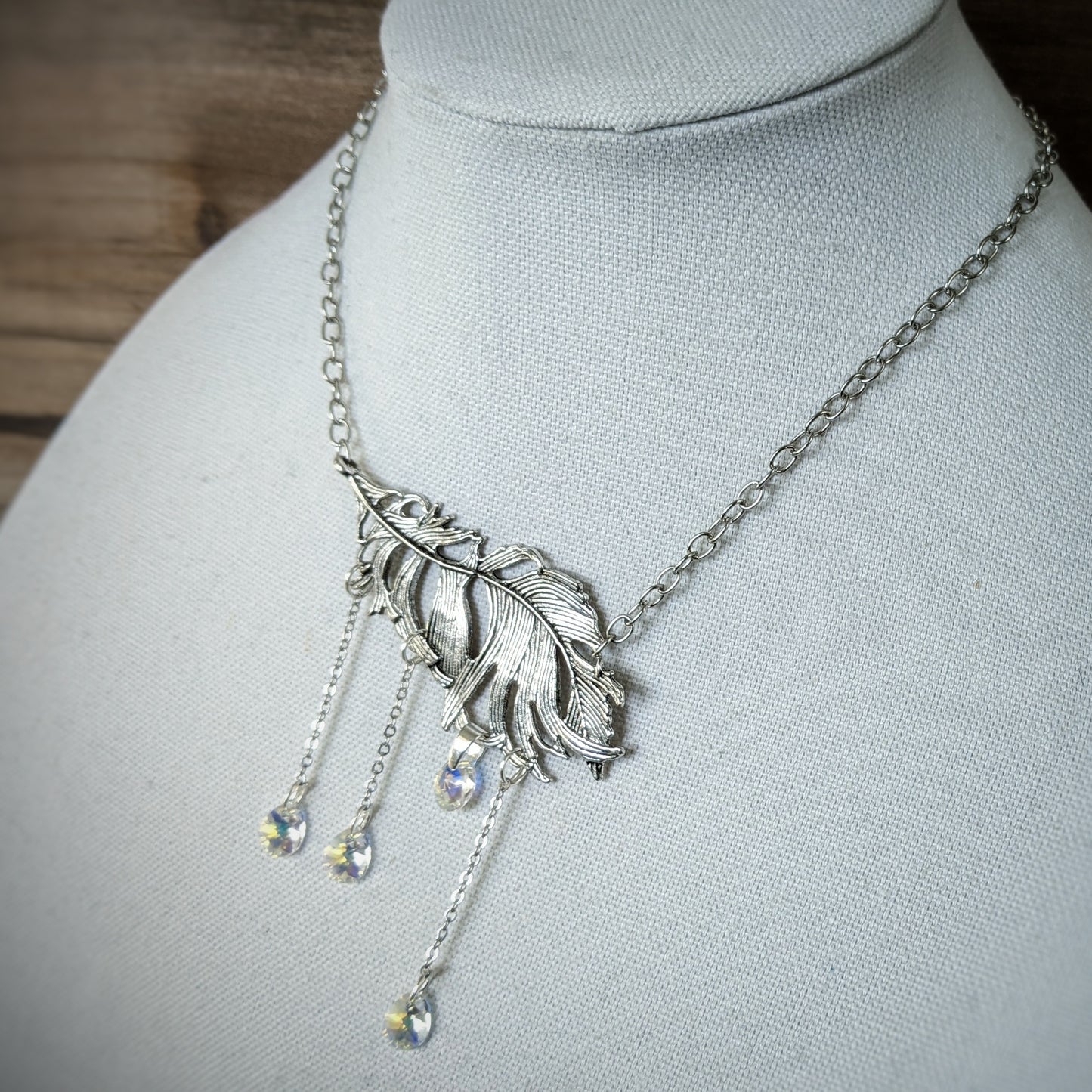 A silver necklace with a large silver leaf focal and crystal drops hanging from it.