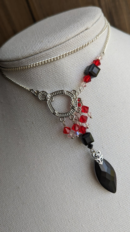 A silver slider necklace with black and red crystals is wrapped like a choker around a fabric bust.