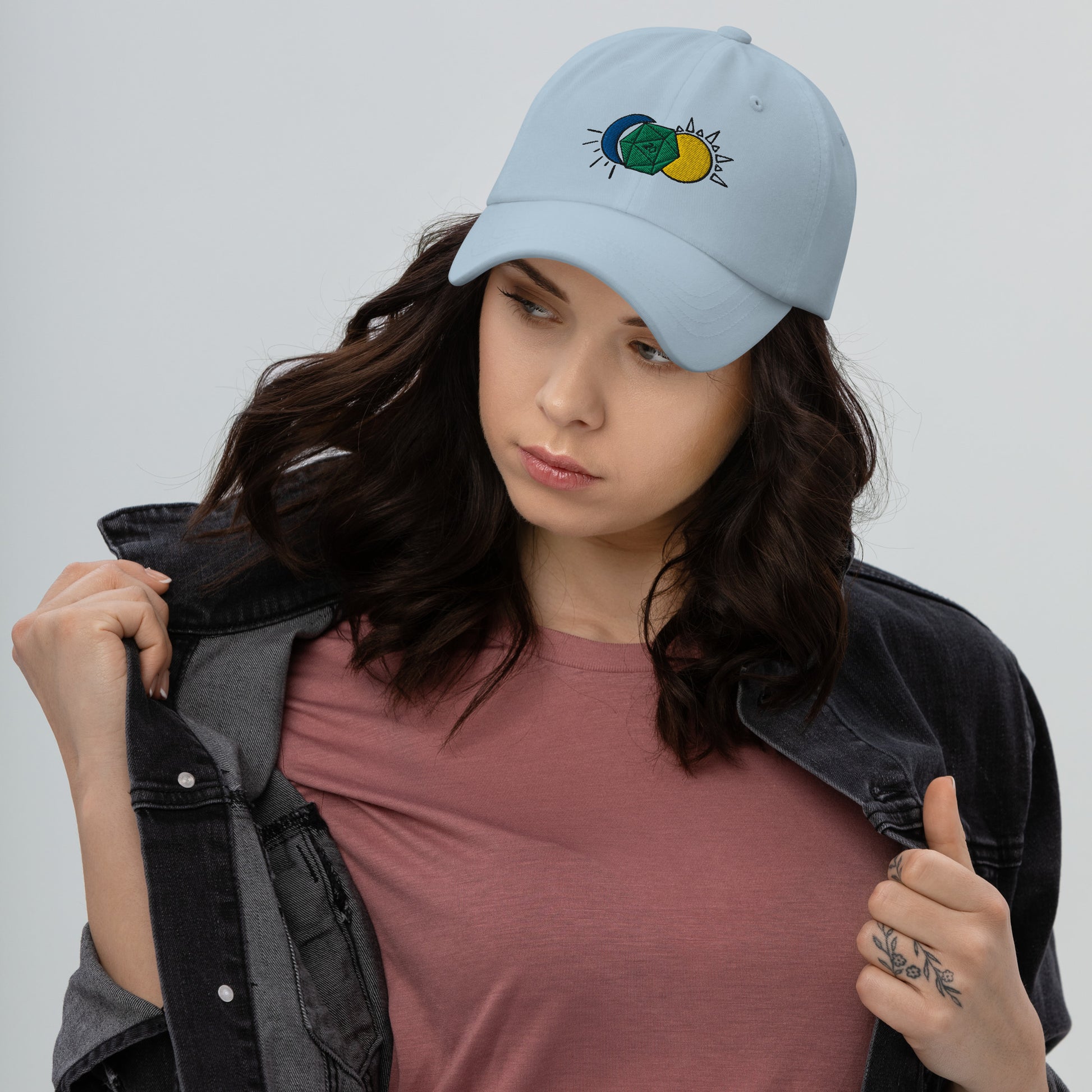 A model wears the Celestial D20 hat in blue, featuring a green D20 flanked by a blue moon and a yellow sun.