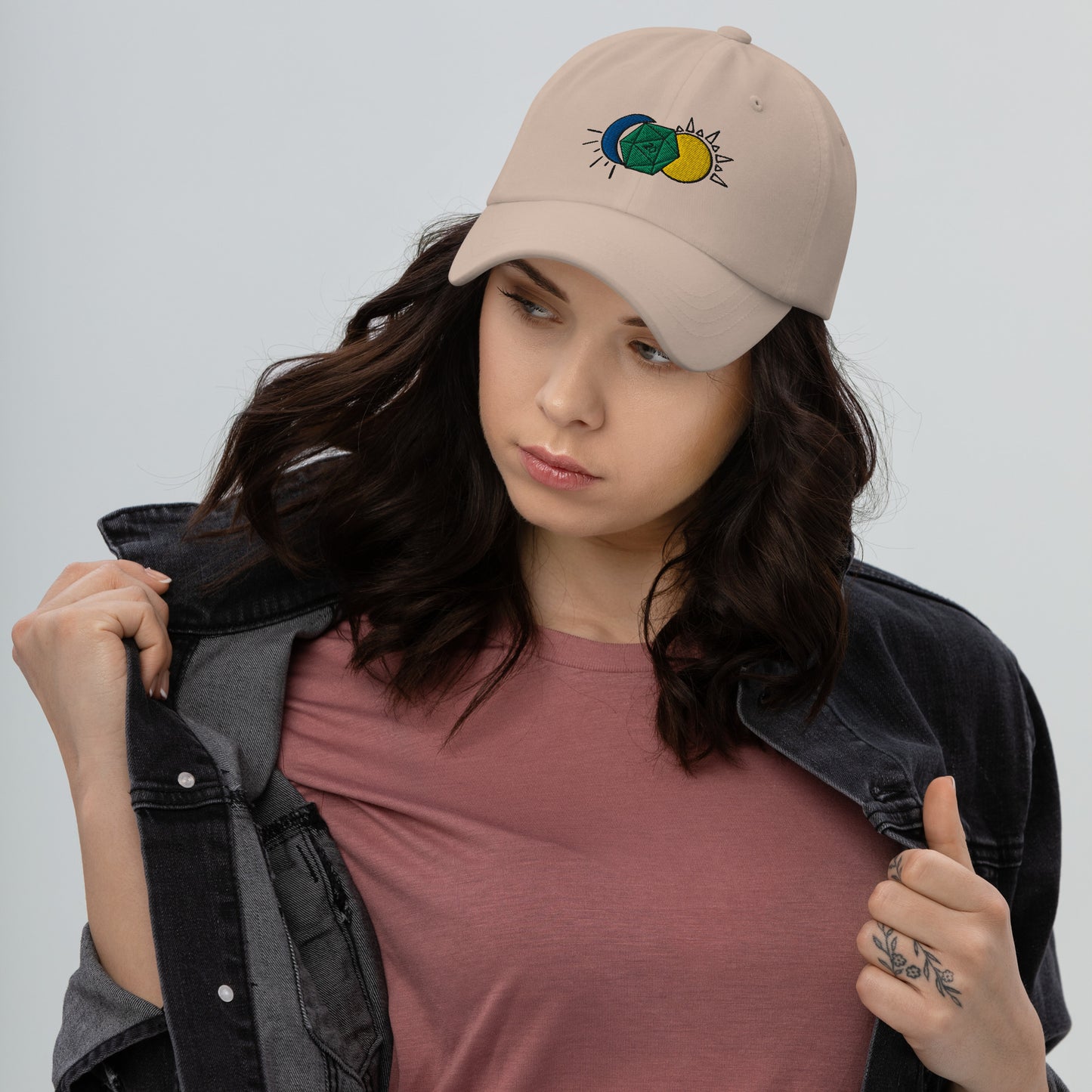 A model wears the Celestial D20 hat in tan, featuring a green D20 flanked by a blue moon and a yellow sun.