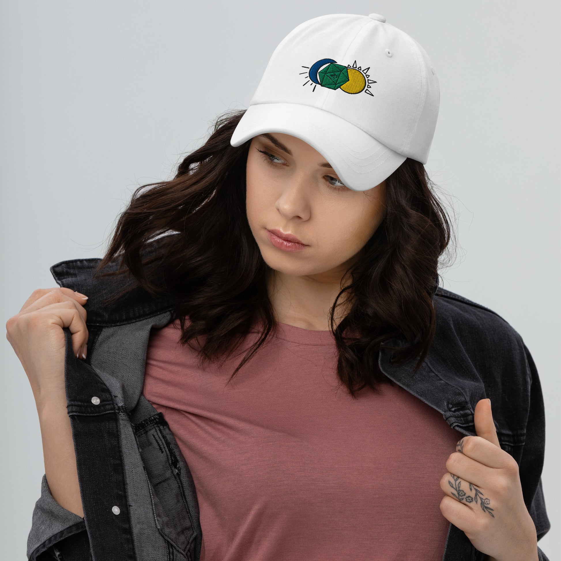 A model wears the Celestial D20 hat in white, featuring a green D20 flanked by a blue moon and a yellow sun.