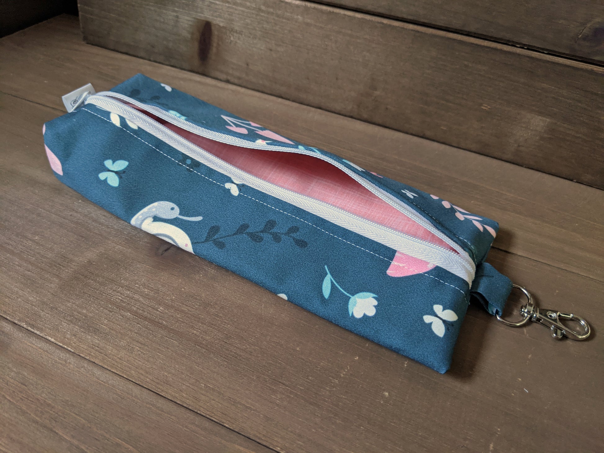 A zippered bag with navy fabric featuring pastel garden bugs sits on a wooden surface.