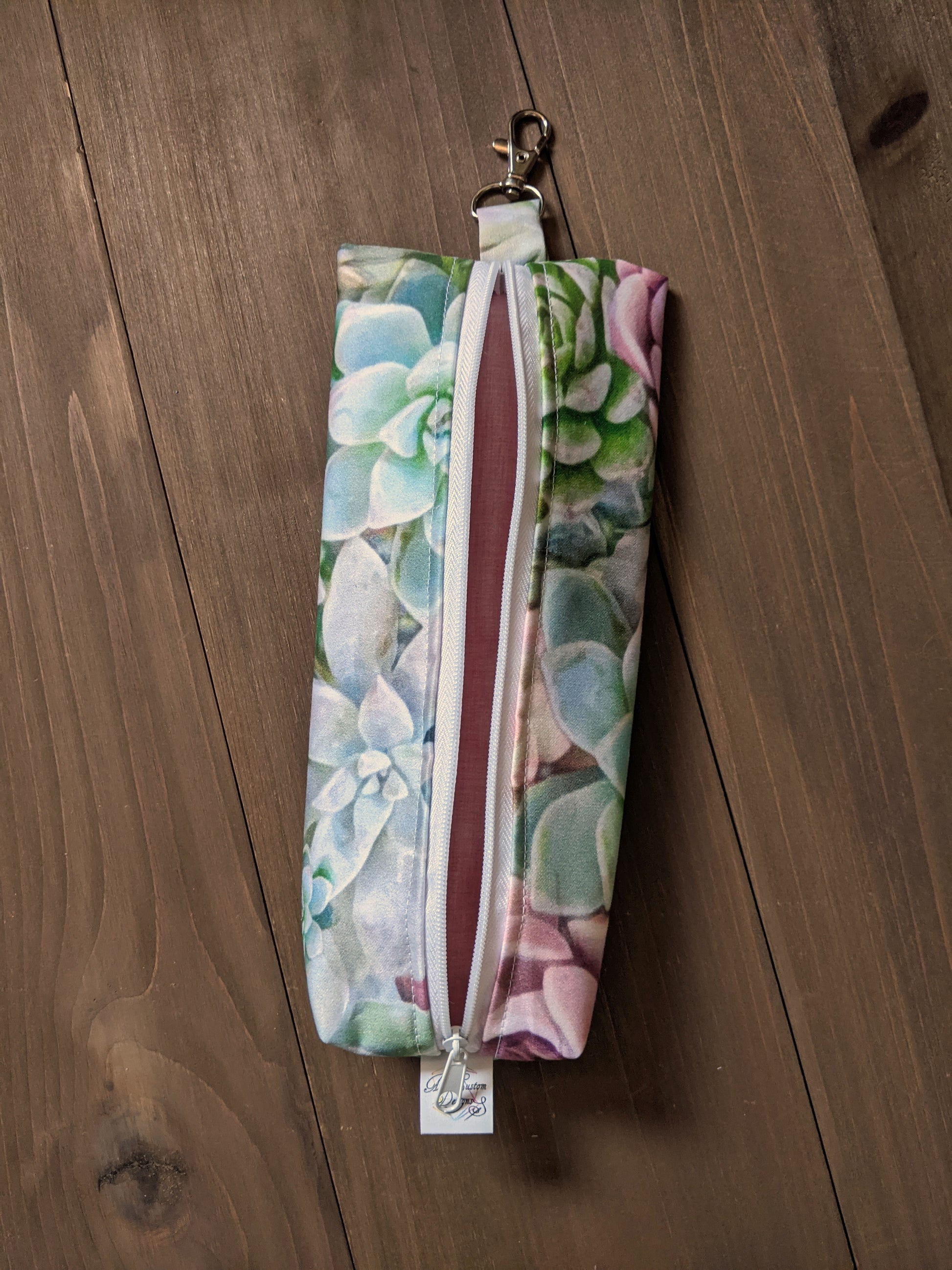 A zippered bag with pastel succulent fabric sits on a wood surface.